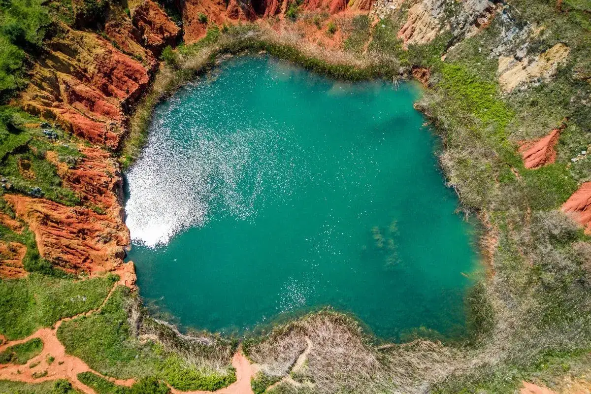 Un suggestivo lago di bauxite in Puglia, con acque turchesi circondate da rocce rosse e vegetazione rigogliosa.