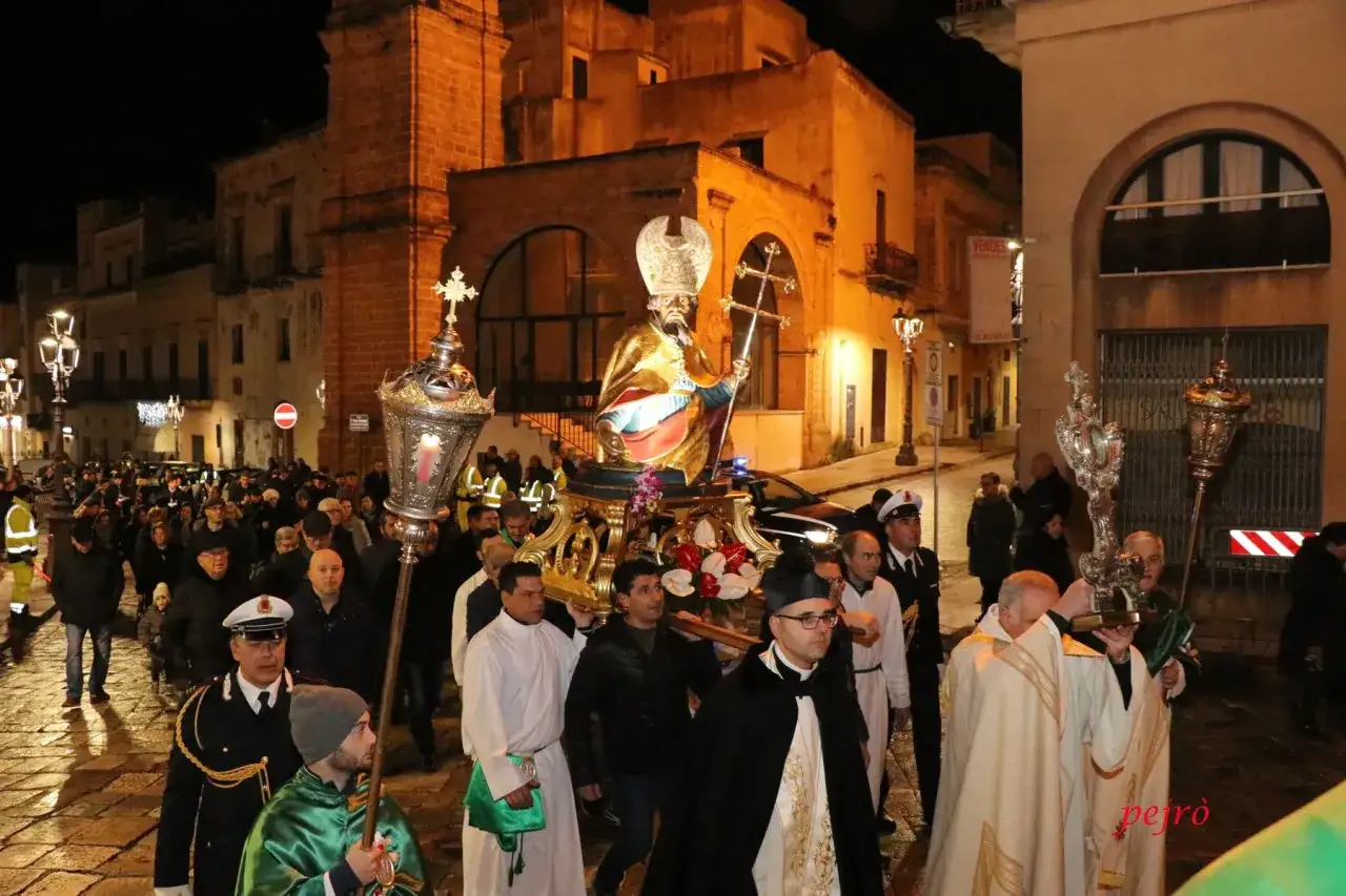 Processione notturna con statua dorata, portatori e fedeli. Un evento tipico delle sagre e feste in Puglia, tra luci e architetture storiche.