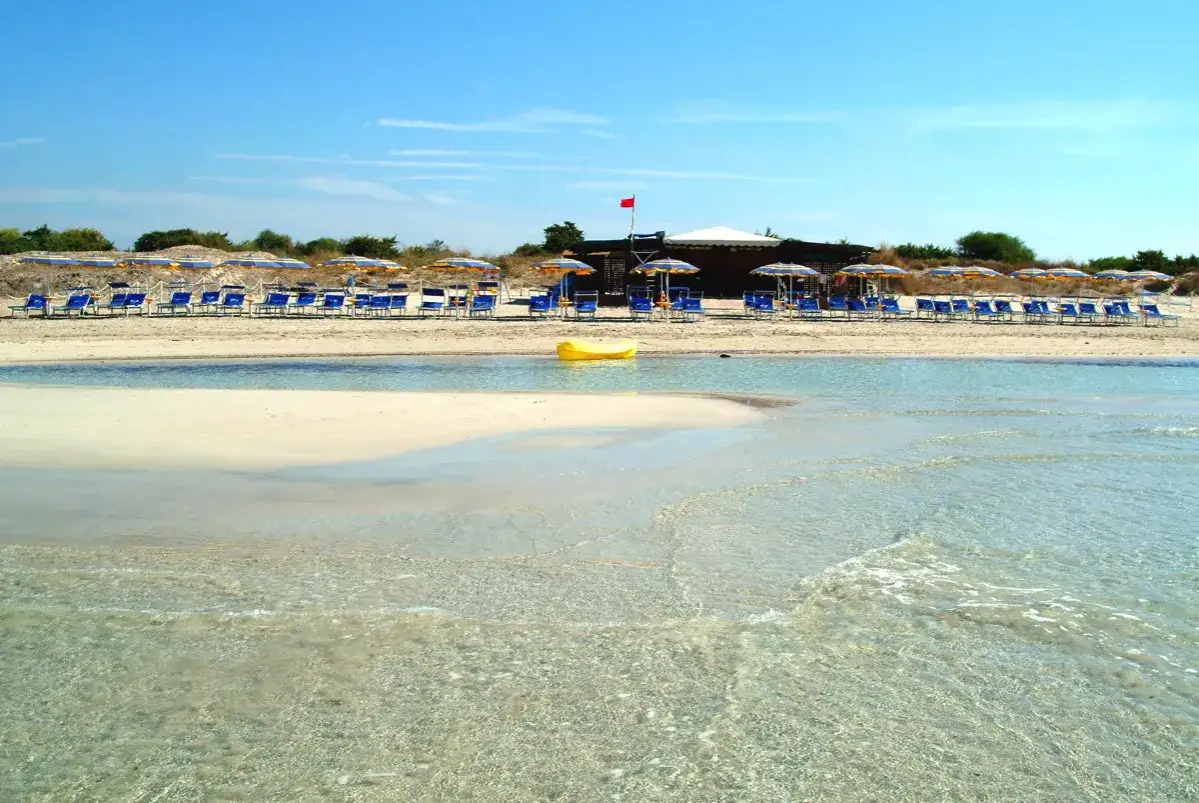 Spiaggia attrezzata con lettini e ombrelloni vicino a Torre San Giovanni. Una canoa gialla galleggia nell'acqua cristallina.