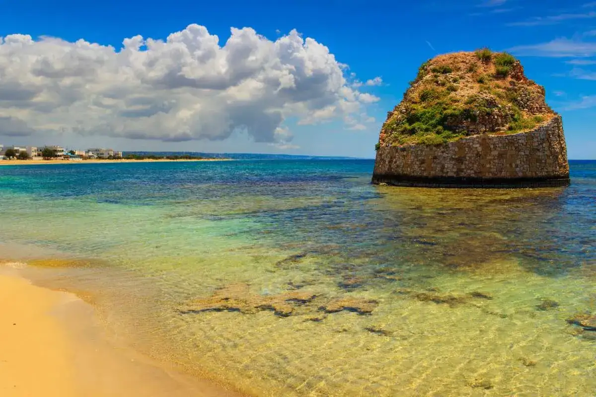 Spiaggia dorata e mare cristallino vicino all'isola della fanciulla, con un'antica torre in pietra che emerge dalle acque turchesi.