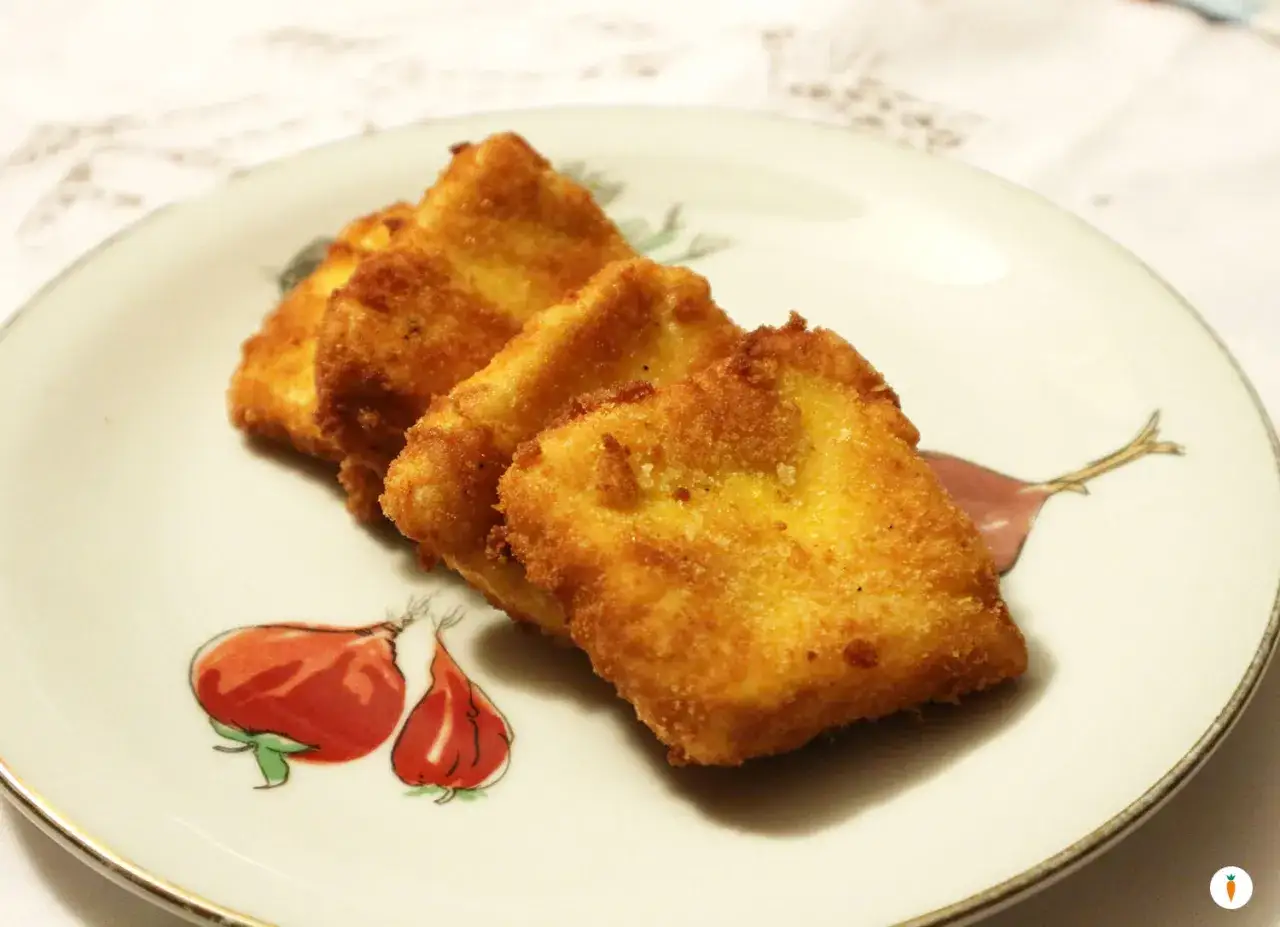 Tre triangoli dorati di ricotta fritta salentina, croccanti fuori e morbidi dentro, serviti su un piatto con disegni di cipolle rosse.