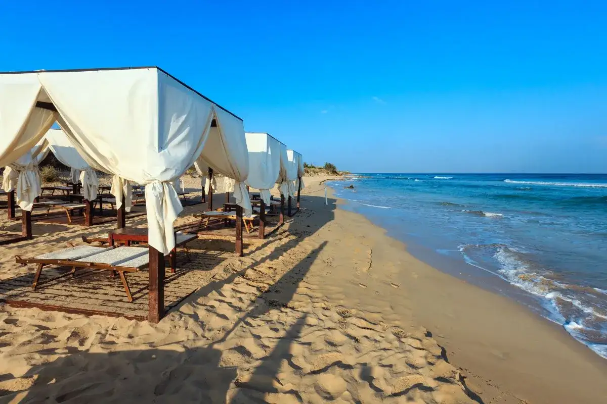 Spiaggia di Pescoluse con lettini e gazebo bianchi, mare azzurro e sabbia dorata. Ecco cosa vedere a Pescoluse per una vacanza indimenticabile.