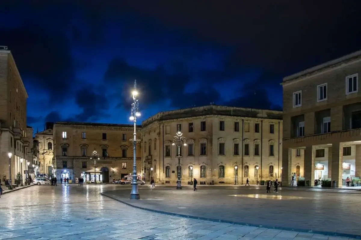 Piazza Carmelo Bene a Lecce di notte, con edifici storici illuminati e il cielo blu intenso.