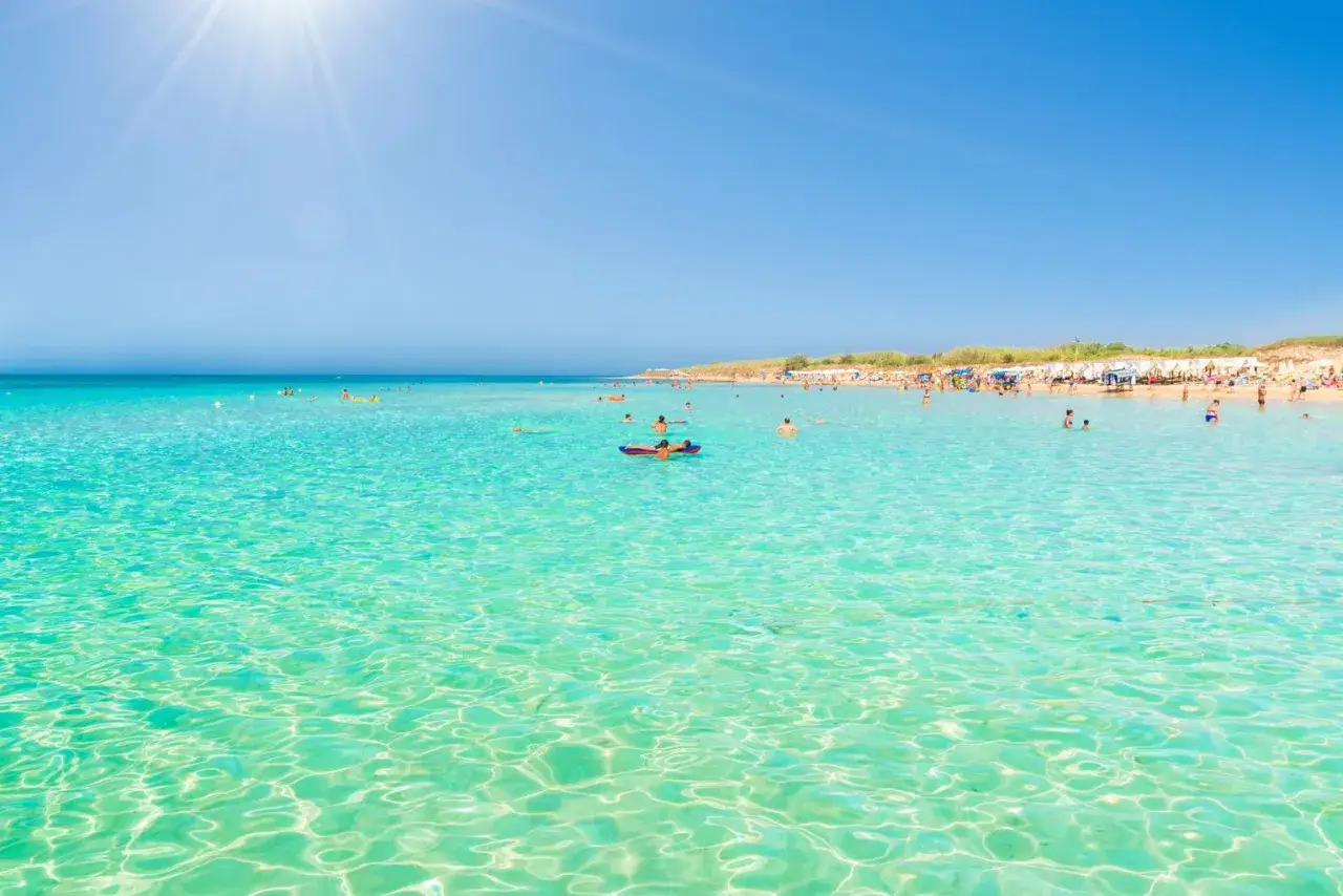 Acque cristalline e sole splendente alle Maldive del Salento, dove bagnanti si godono il mare turchese e la spiaggia affollata.