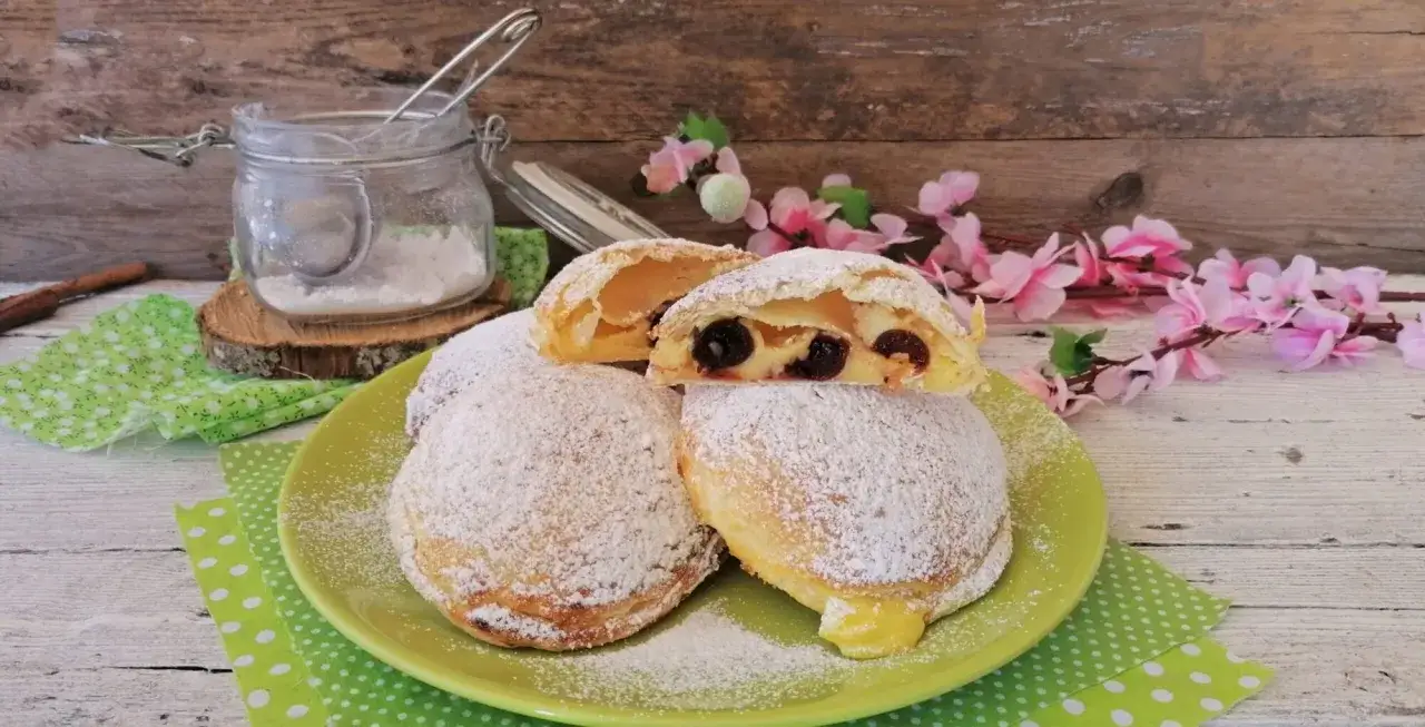 Monachine salentine dolci e profumate, con ciliegie e crema, cosparse di zucchero a velo su un piatto verde.