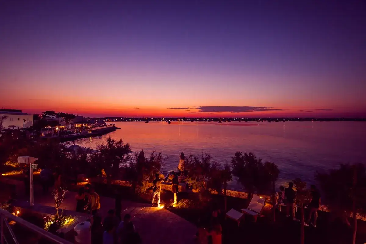 Tramonto mozzafiato sul mare, perfetto per decidere cosa fare stasera in Puglia. Ristoranti illuminati e gente che passeggia.