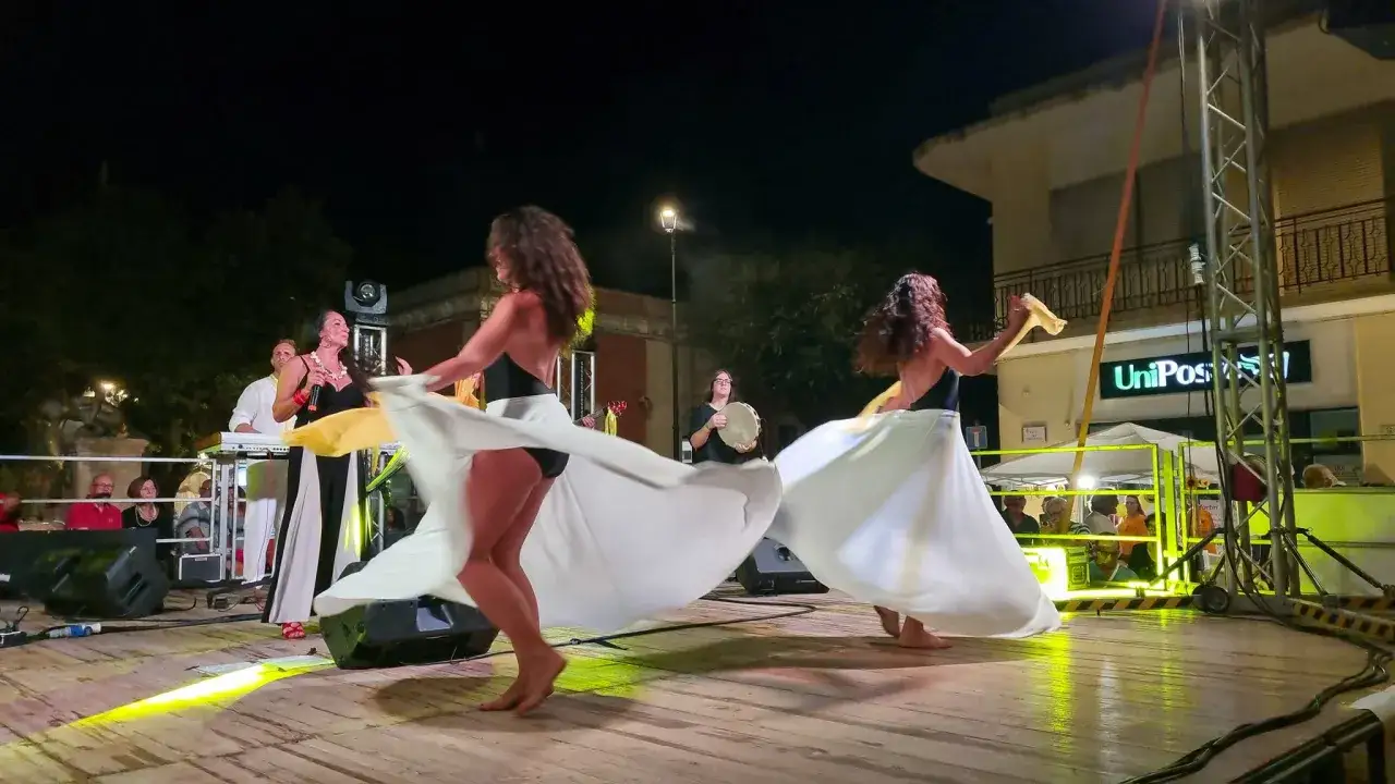 Ballerine con ampie gonne bianche danzano sul palco durante eventi Salento. Cantante e musicisti animano la serata.