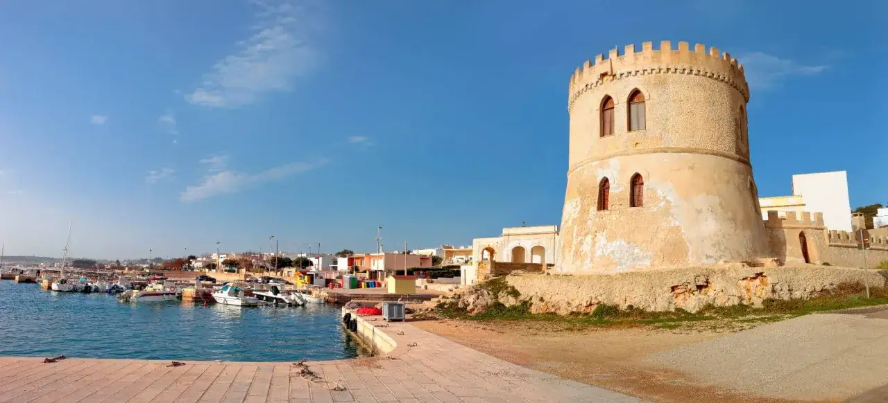 Torre Vado, un antico torrione domina il porto con barche ormeggiate e case colorate sotto un cielo azzurro.