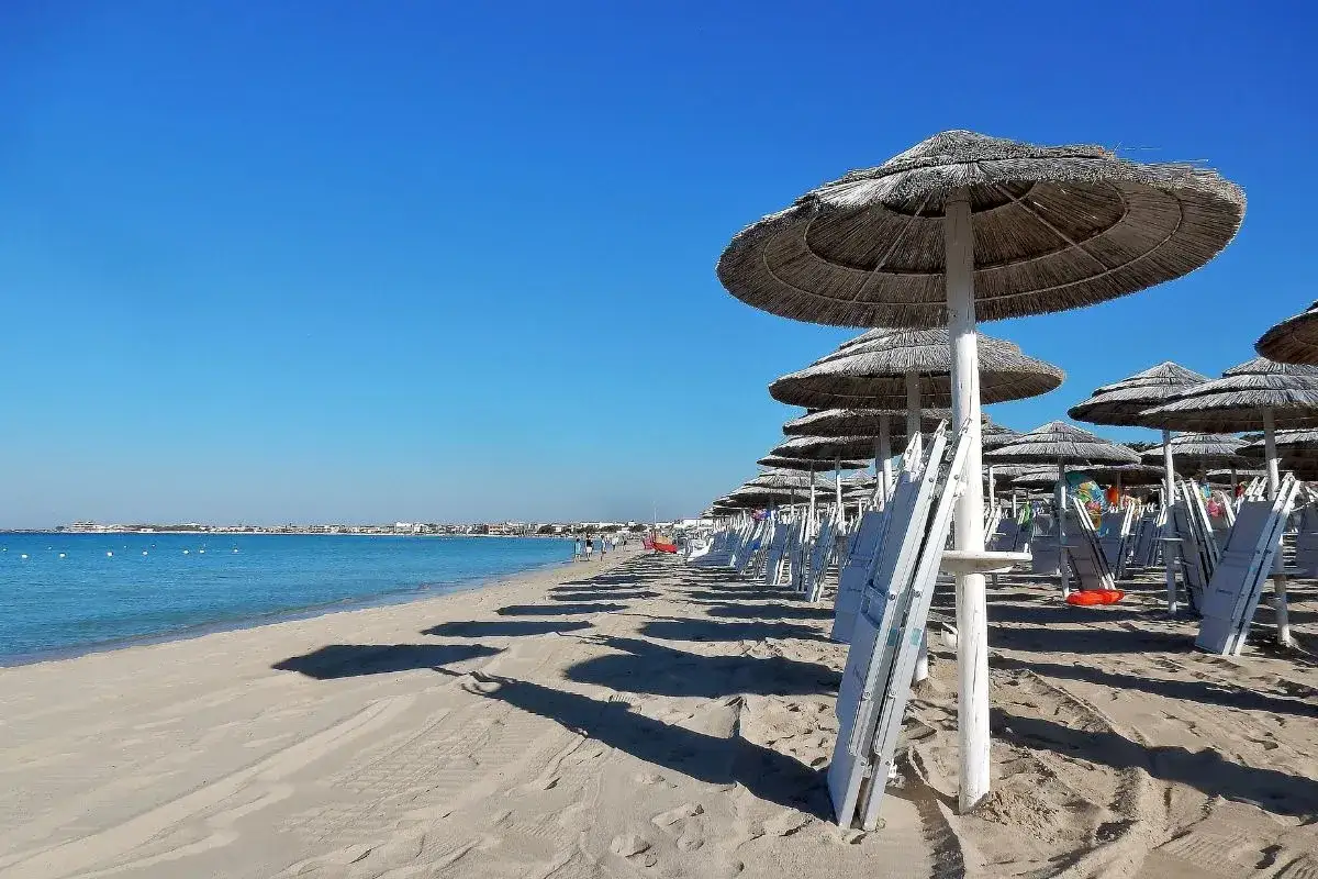 Ombrelloni di paglia e lettini bianchi su una spiaggia sabbiosa, con il mare azzurro e il cielo limpido. Il miglior lido Torre Lapillo offre relax e comfort.