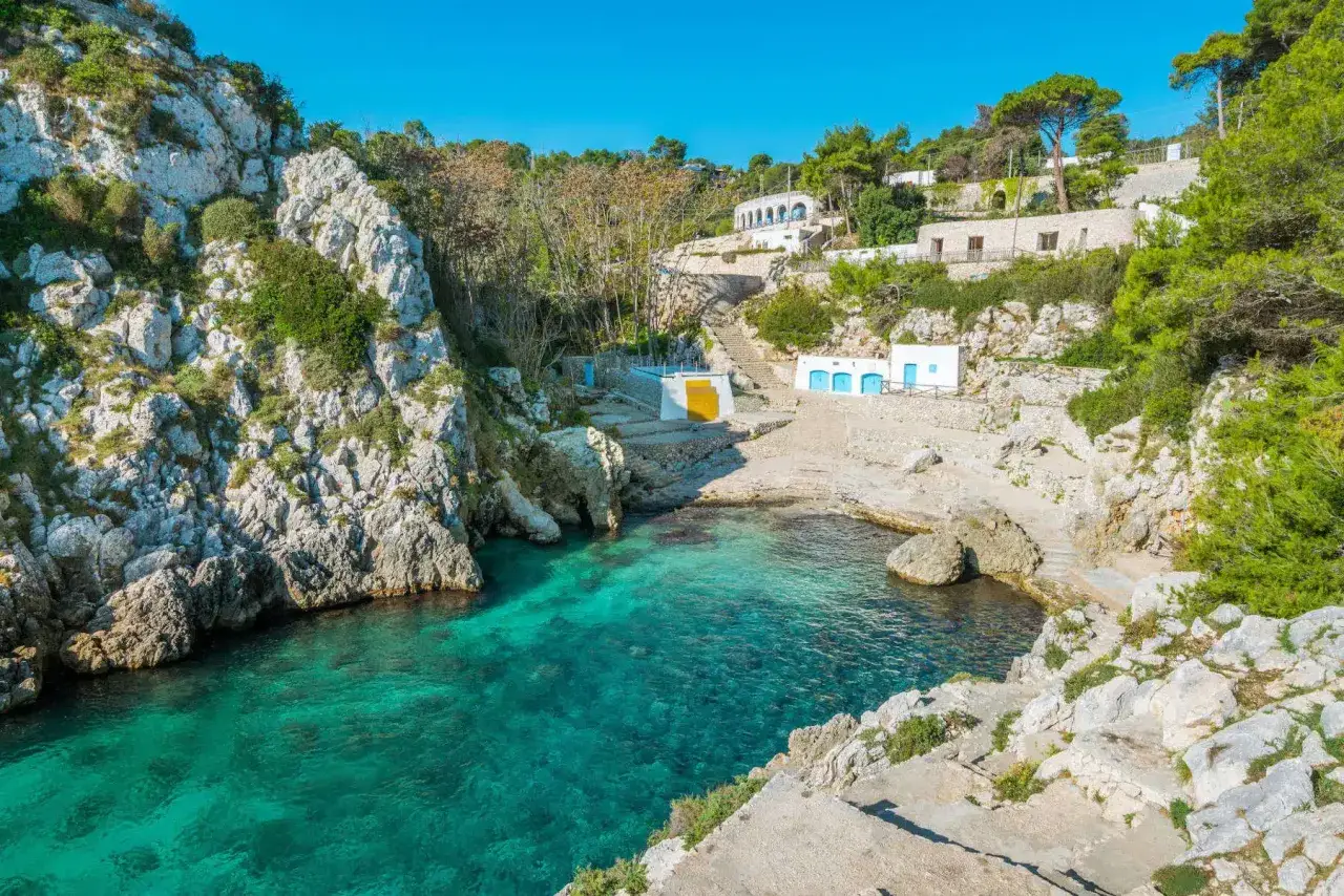 Baia incantevole con acque cristalline, rocce bianche e piccole case bianche con porte blu, un angolo di paradiso tra i borghi pi&ugrave; belli d'Italia in Puglia.
