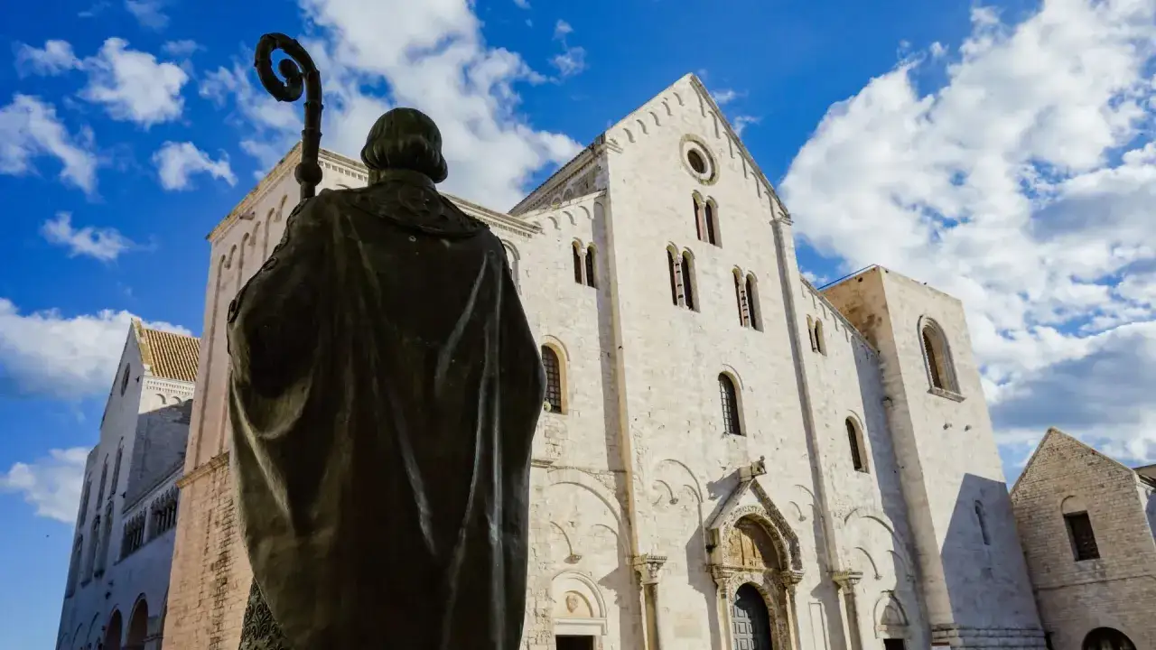 Statua di San Nicola davanti alla Basilica, un luogo imperdibile da vedere a Bari. Cielo azzurro e nuvole bianche.