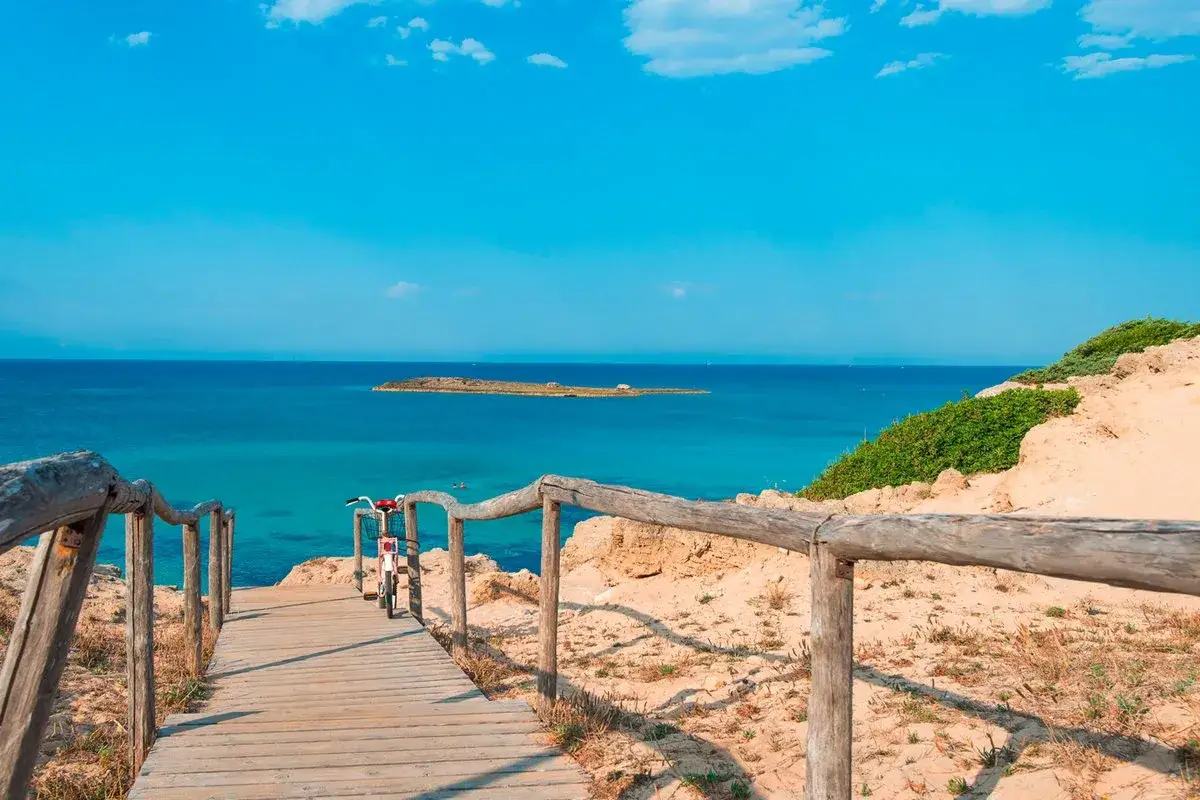 Sentiero in legno verso il mare cristallino di Ugento. Un'isola in lontananza e un'aria di vacanza.