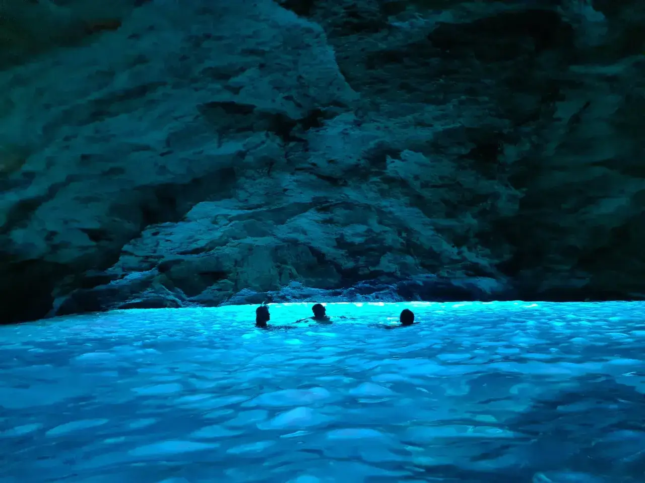 Persone nuotano nelle acque cristalline di una grotta nel Salento, illuminate da una luce blu intensa che riflette sulle rocce.