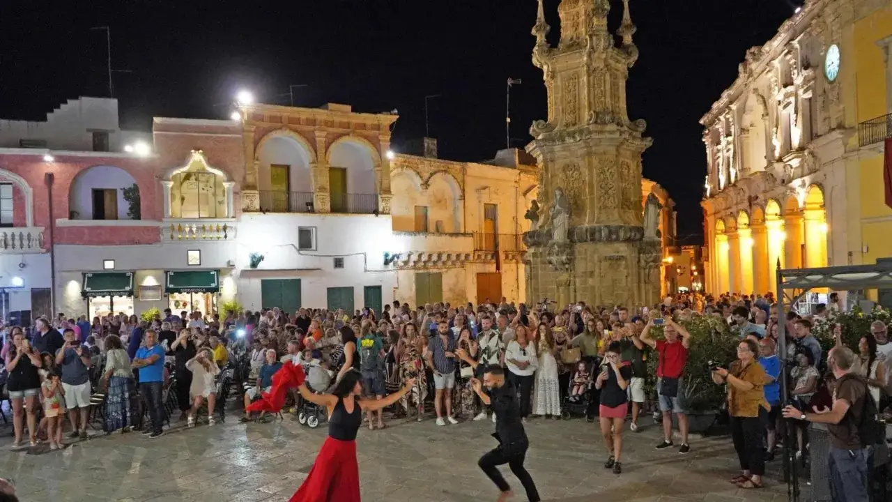 La piazza si anima per la sagra della taranta con ballerini e folla festante.