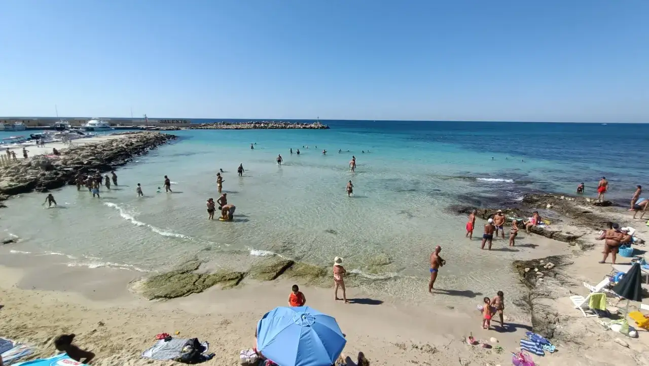 Spiaggia affollata vicino alla torre vado pescoluse, con gente che nuota e si rilassa al sole.