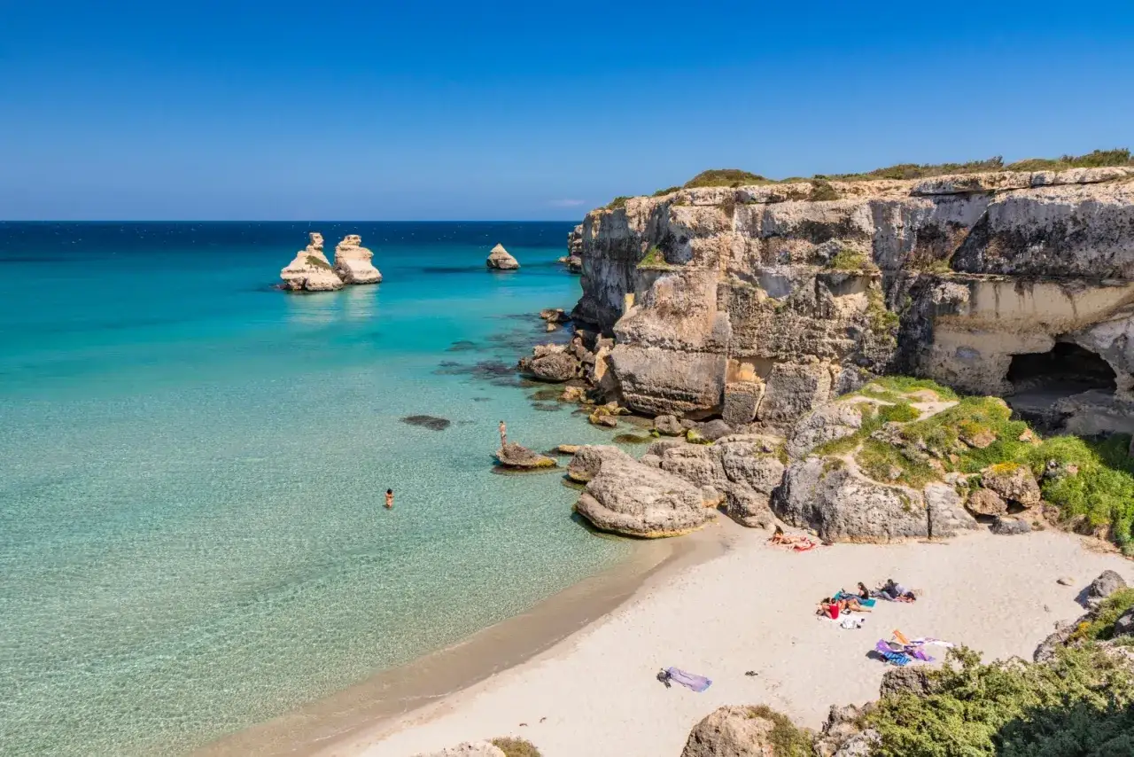 Spiaggia di Torre dell'Orso con faraglioni e scogliere calcaree. Acque cristalline e gente che si rilassa al sole.