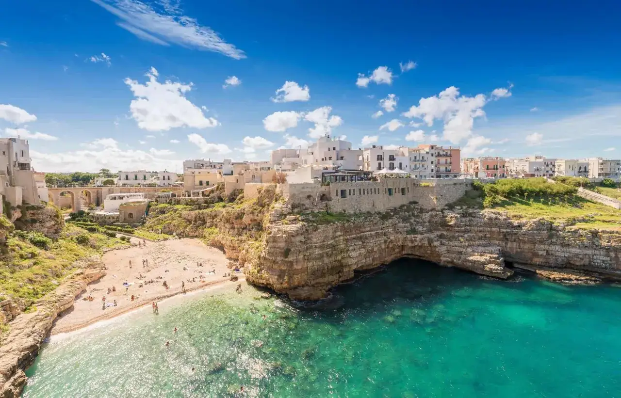 Un incantevole scorcio di Polignano a Mare, perfetto per un tour Puglia 10 giorni. Spiaggia dorata, mare cristallino e case bianche a picco sul mare.