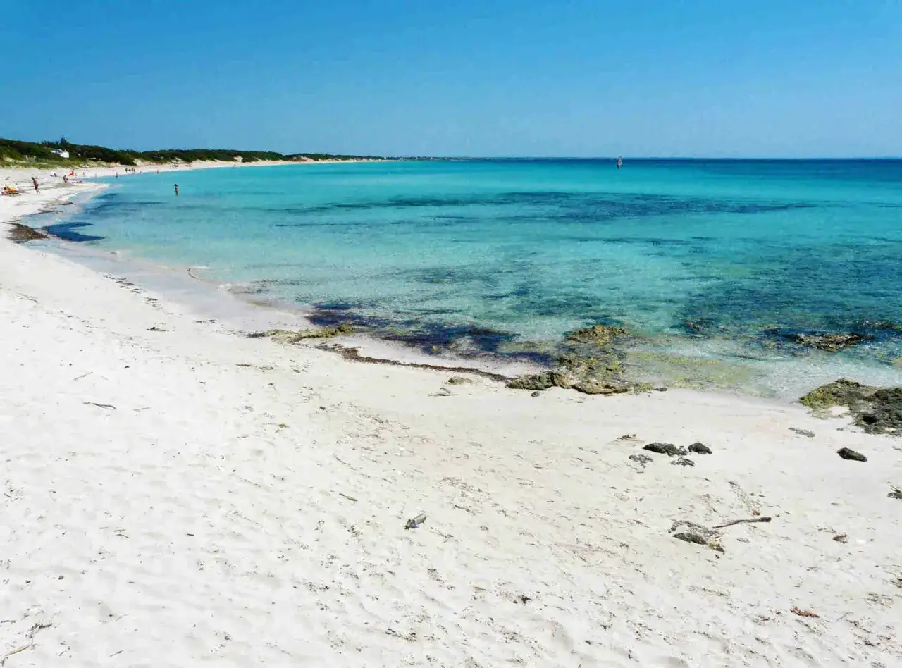 Spiaggia bianca e mare cristallino in Puglia, con acque turchesi e trasparenti che invitano a un tuffo.
