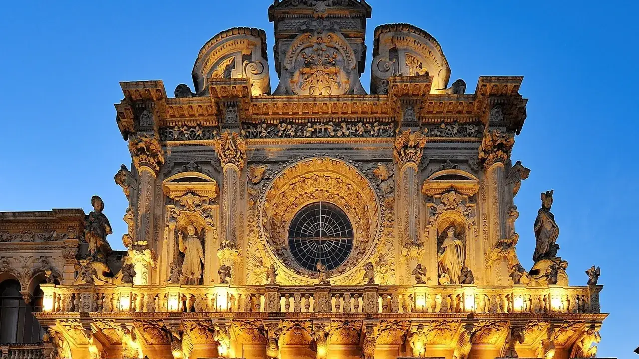Facciata barocca illuminata a Lecce, un capolavoro tra le cose da fare a Lecce. Statue e rosoni decorano l'edificio.