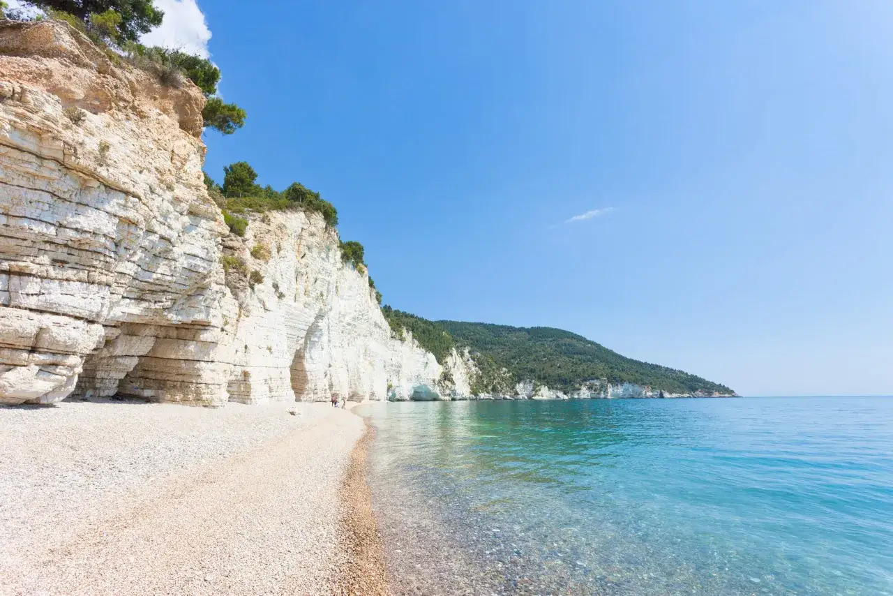 Spiaggia di ciottoli con scogliere bianche e mare cristallino, ideale per i mete puglia estate.