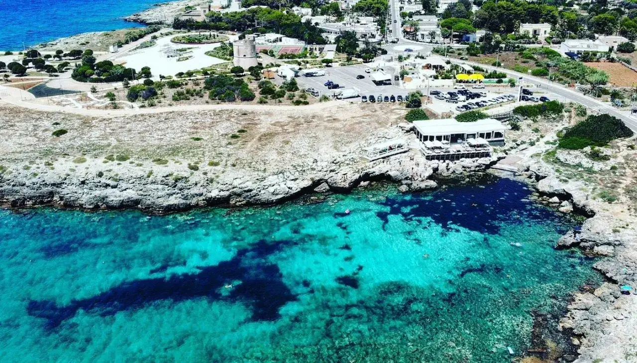 Torre sulla costa rocciosa, con mare cristallino e una piccola spiaggia sabbiosa in lontananza.