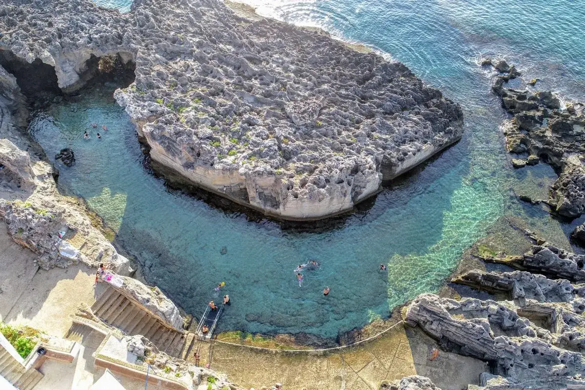 Tricase: cosa vedere? Una baia rocciosa con acque cristalline e persone che nuotano. Perfetta per un tuffo rinfrescante.
