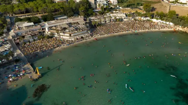 Vista aerea di una spiaggia affollata con ombrelloni e persone che nuotano nel mare cristallino, una delle spiagge più belle del mare di Taranto.