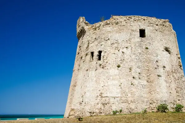 Antica torre mozza, con merli frastagliati, si erge contro un cielo blu intenso, testimone silenzioso di antiche storie.