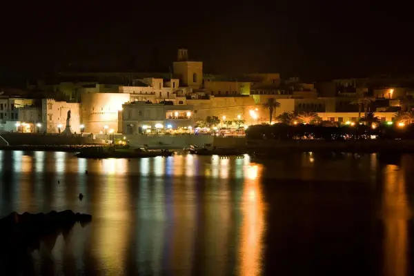 Otranto di notte: luci, castello e riflessi sull'acqua. La città si anima, pronta per le discoteche estive.