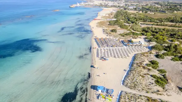 Spiaggia di Torre San Giovanni con ombrelloni e lettini, mare cristallino e vegetazione mediterranea.