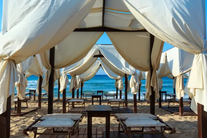 Tende bianche su una spiaggia dorata, con il mare azzurro sullo sfondo. Un angolo di paradiso che ricorda le Maldive del Salento, pronto per il relax.
