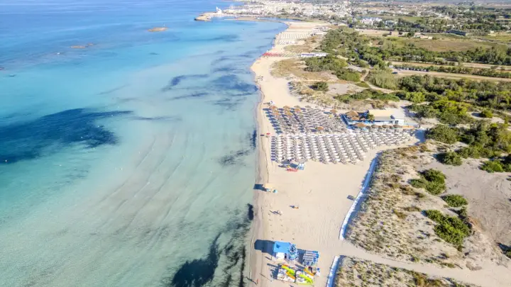 Spiaggia di Torre San Giovanni con ombrelloni e lettini, mare cristallino e vegetazione mediterranea.