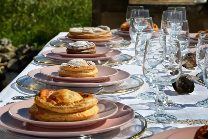 Tavola apparecchiata con bicchieri di cristallo e piatti rosa, su cui riposano dolci invitanti, tra cui una piscialetta leccese cosparsa di zucchero a velo.