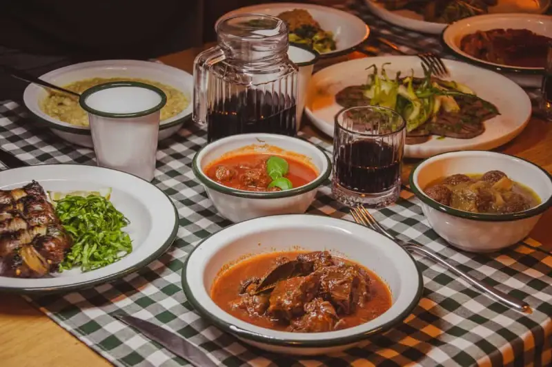 Tavola imbandita in una trattoria tipica salentina con vari piatti di carne e contorni, accompagnati da vino rosso.